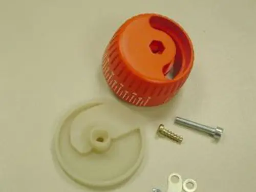 Set bestehend aus einem orangefarbenen Luftregulierungsknopf und verschiedenen Schrauben, passend für Produkte der Marke Remeha. Teile liegen auf einem hellen Untergrund.